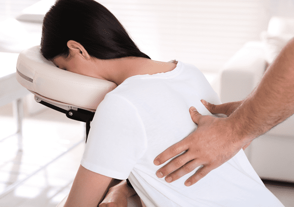 A woman receiving a massage in a chair designed for massage from a massage therapist at a corporate event