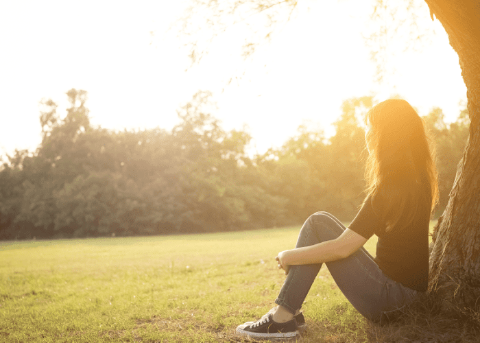 A woman sitting by a tree after her massage session to reduce her symptoms of depression